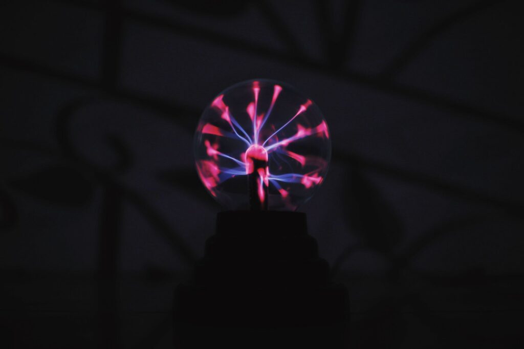 From below of bright glowing plasma ball with electric purple lights placed in dark room in daytime