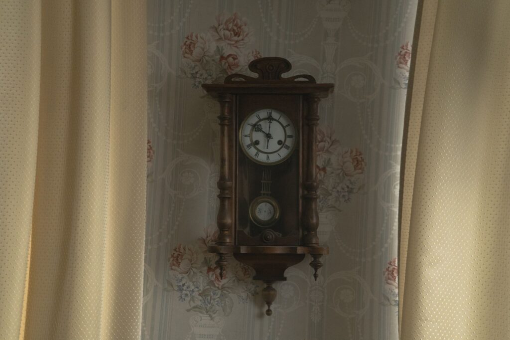 A vintage pendulum wall clock surrounded by floral wallpaper with curtains.