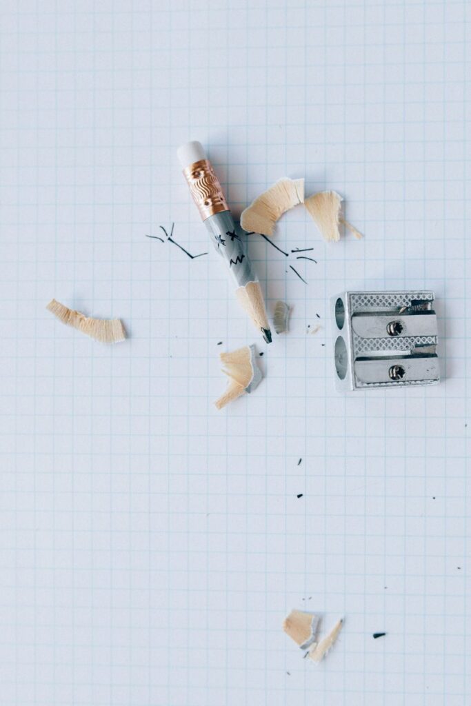 Graph paper with a sharpened pencil and shavings around a dual sharpener, top view.